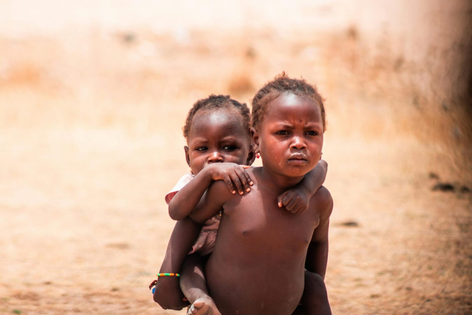 Two children are standing in the dirt.