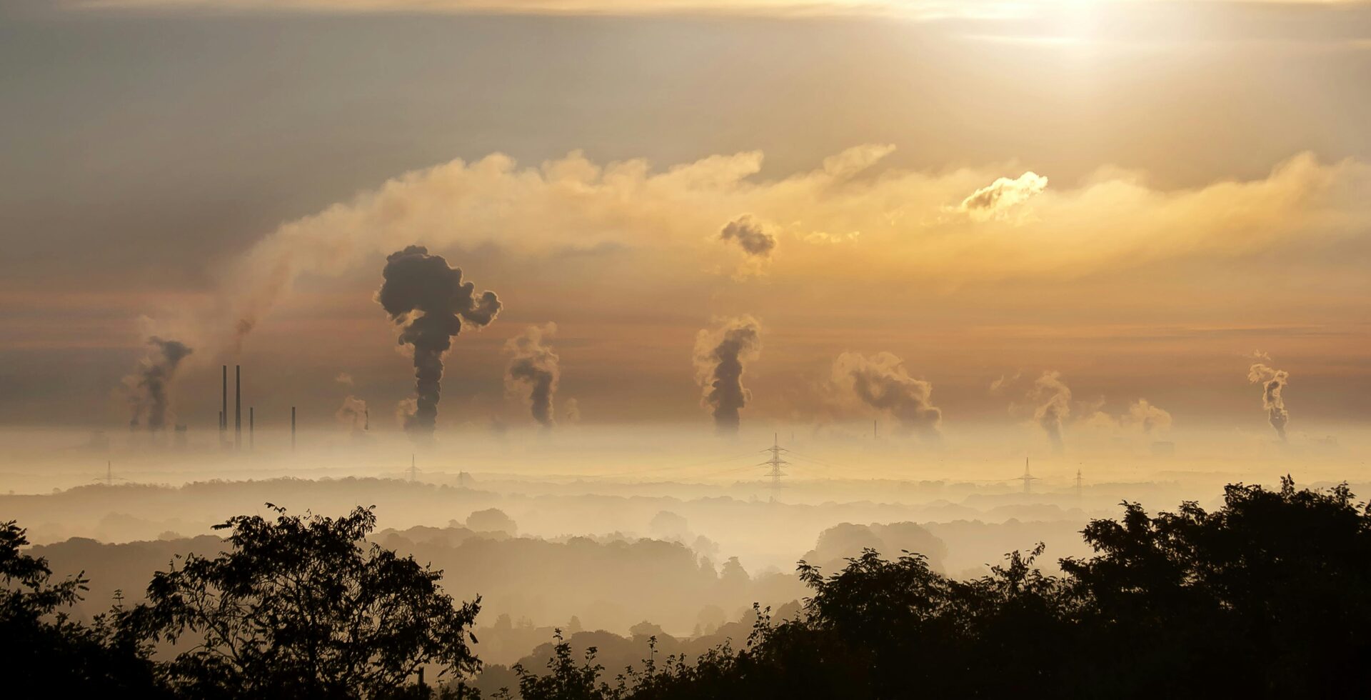 A view of the sun setting over some smoke stacks.